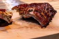 Glazed American BBQ – Honey Pork Ribs on a wooden board, one piece cut open showing the bone.
