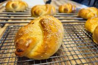 Golden Pletýnka Bun topped with sesame seeds cooling on a wire rack next to smaller buns