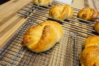 Golden braided Pletýnka Buns topped with sesame seeds cooling on wire racks over a wooden counter.