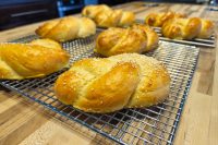 Golden braided Pletýnka Bun rolls, some topped with sesame seeds, cooling on wire racks.
