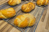 Golden braided Pletýnka Buns with sesame seeds cooling on wire racks over a wooden table.