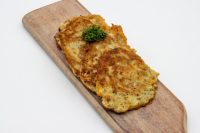 Two golden fried Side Potato Pancakes Bramboráčky on a wooden board with a parsley sprig.