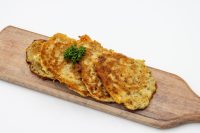 Four golden-fried Side Potato Pancakes Bramboráčky on a wooden board, garnished with a sprig of dill.