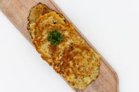 Four golden fried Side Potato Pancakes Bramboráčky on a wooden board with curly parsley garnish.
