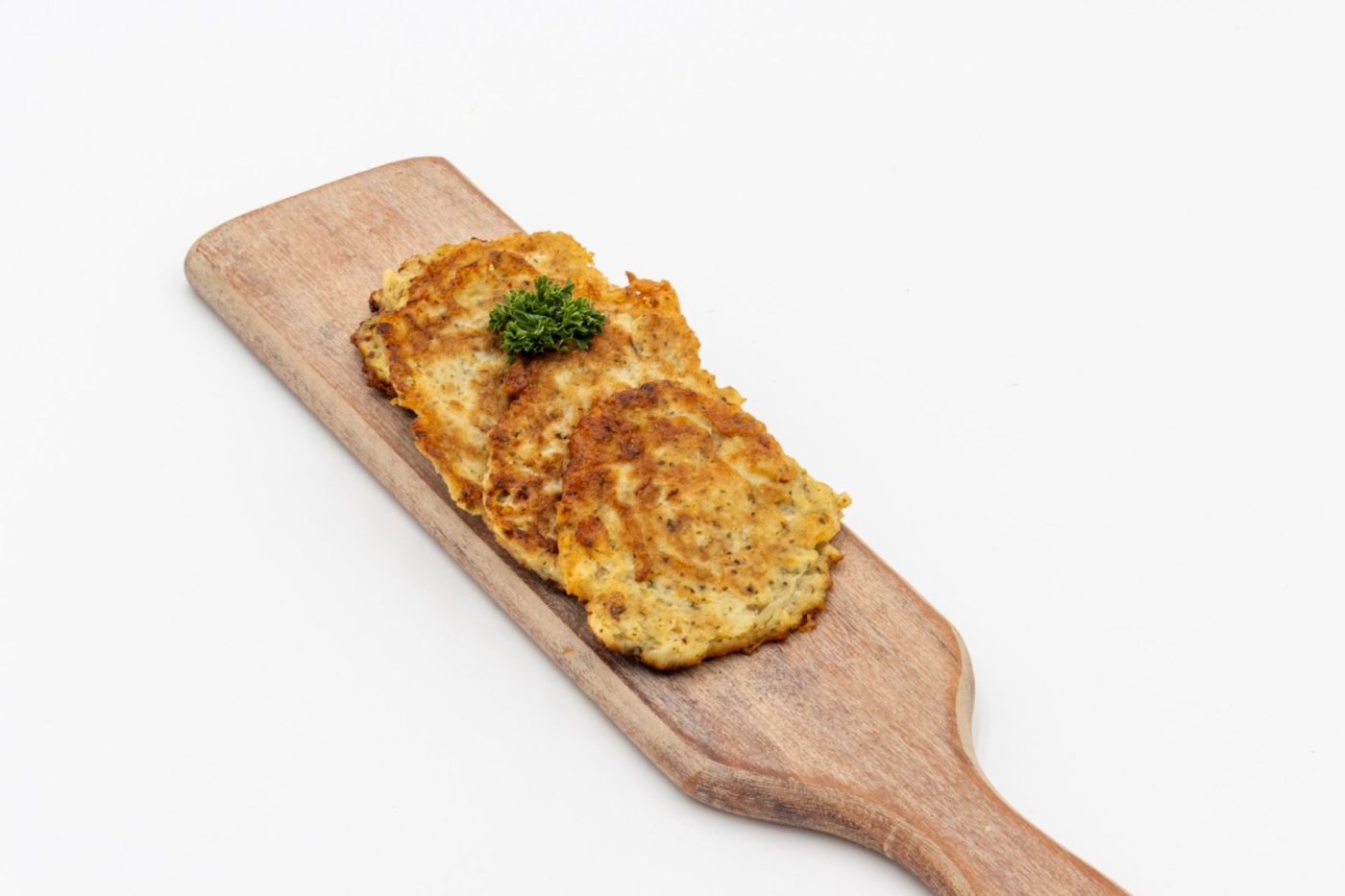Two golden Side Potato Pancakes Bramboráčky stacked on a wooden board with a herb garnish.