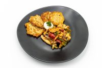 Potato pancakes beside Slovak Meat Sauté Mäsové Soté with peppers, mushrooms, and sour cream on a black plate