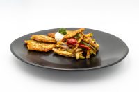 Slovak Meat Sauté Mäsové Soté with peppers, onion, and sour cream beside potato cakes on a black plate