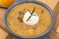 Bowl of Valašská Kyselica Soup topped with a sour cream dollop and a rosemary sprig, with mushrooms and diced potato visible in the broth.